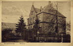 Ansicht des 1901(1902 erbauten Pfarrhauses mit Umzäunung, das Pfarrhaus wurde im Stil der Pfarrkirche nach Plänen des Architekten Heintz aus Koblenz erbaut.